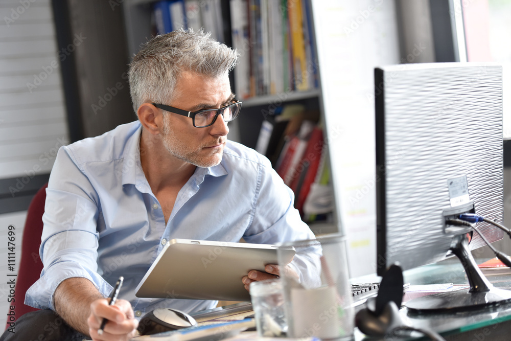 Business owner sitting in office working on tablet