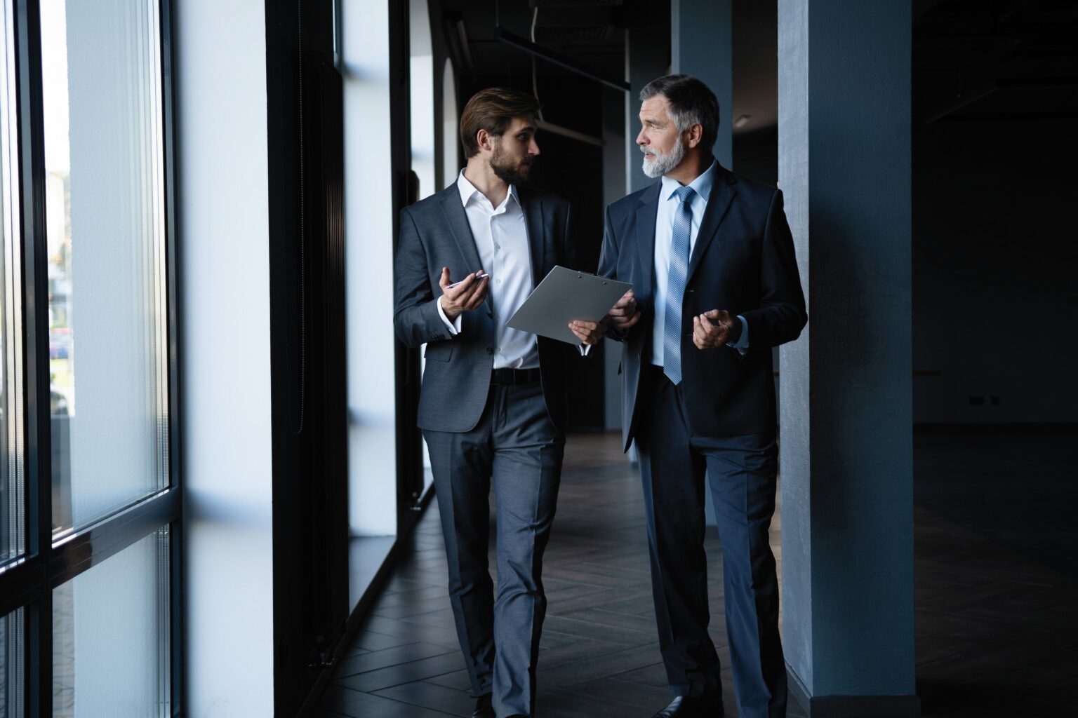 Two colleagues communicating in corridor, partners walking in the modern office